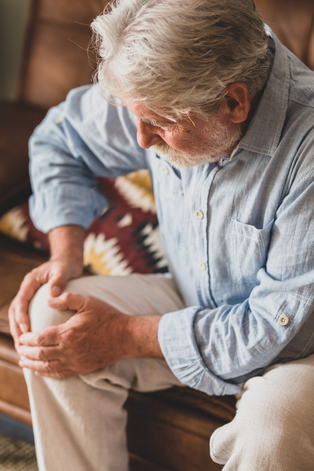 An image of an elderly man sitting with both hands at his right knee. Total and partial knee replacement procedures are surgical interventions to relieve knee pain.